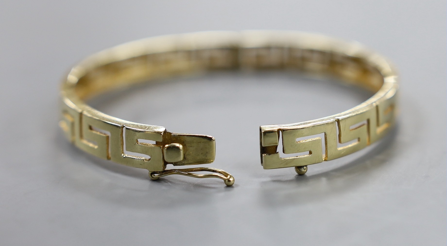 A modern yellow metal hinged bangle with Greek Key decoration and a 9ct donkey and cart charm, gross weight 23.2 grams.